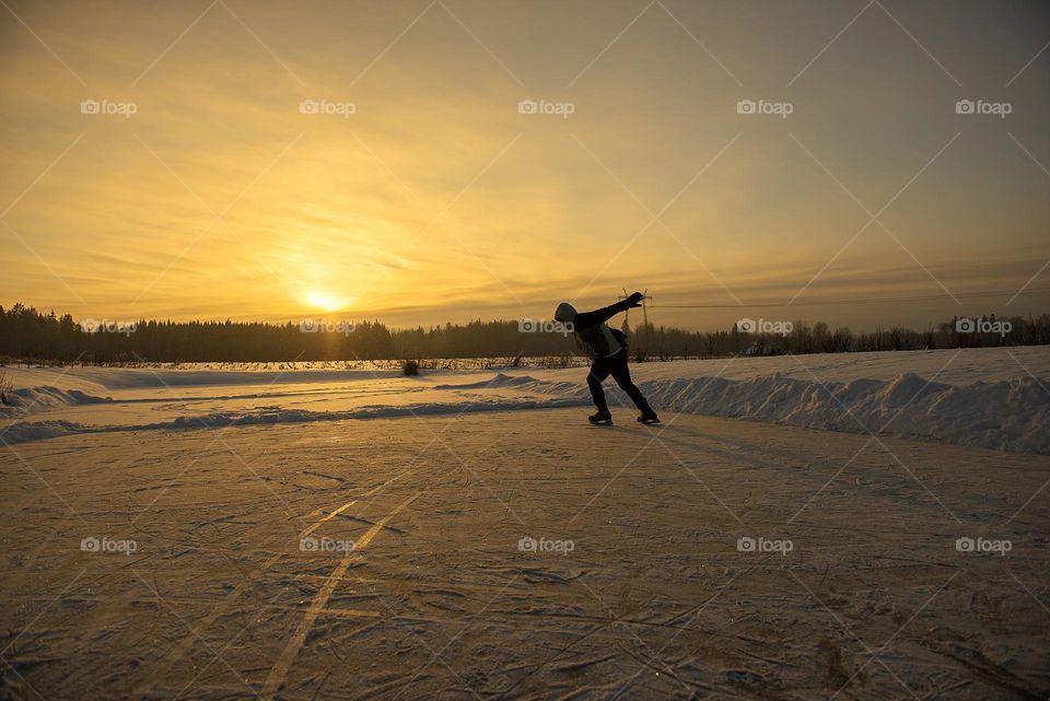 A silhouette of a man skating on a frozen lake at sunset