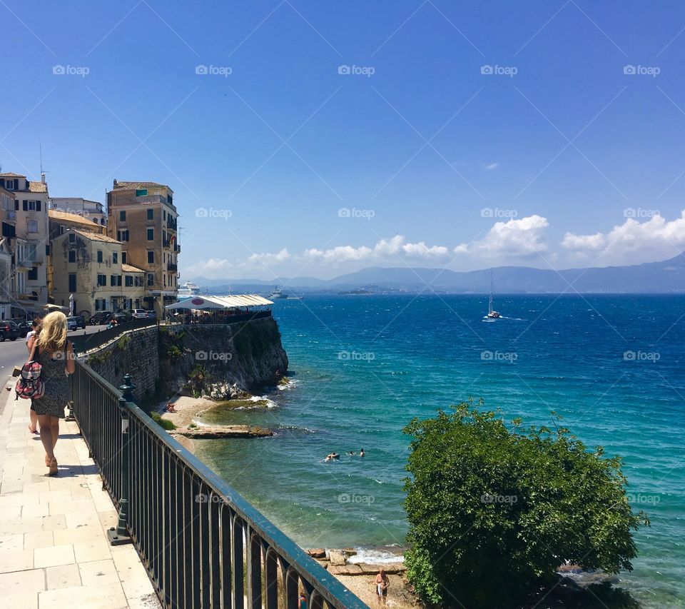 Girl walks along coastal path in Corfu Old Town, Greece