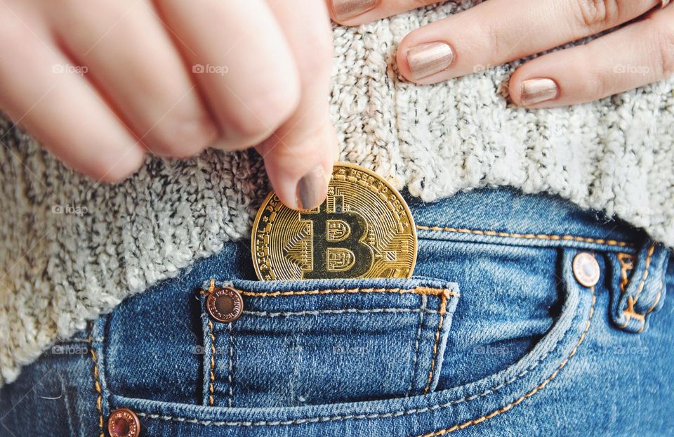 Close-up photo of hand holding golden bitcoin coin and puttin it in pocket of jeans
