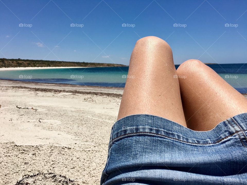 Chilling out at the beach, woman laying on sand, bare legged, wearing denim skirt, point of view