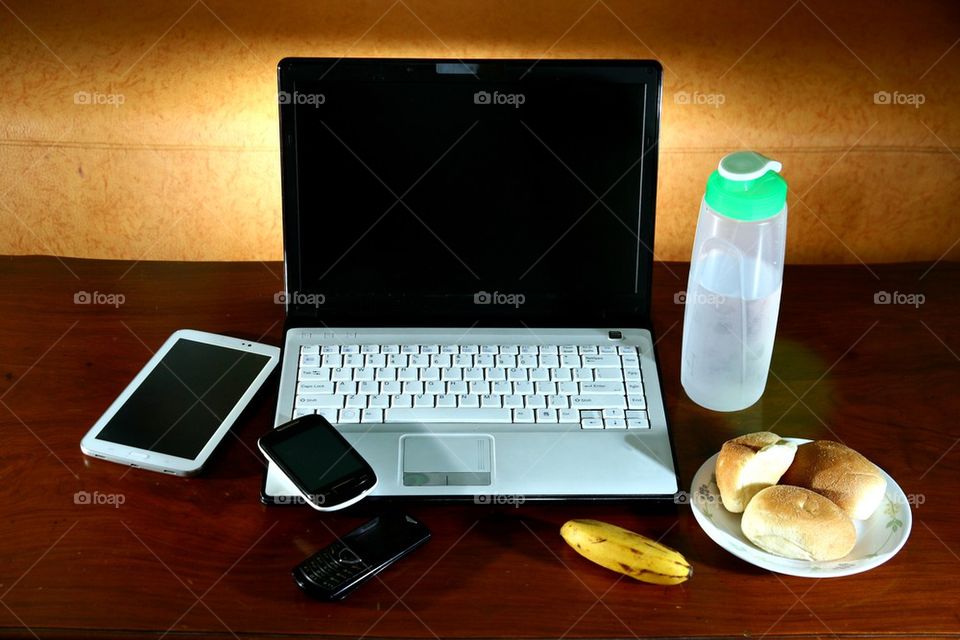 laptop computer, tablet, cellphone, smartphone, banana, water and bread on a living room table