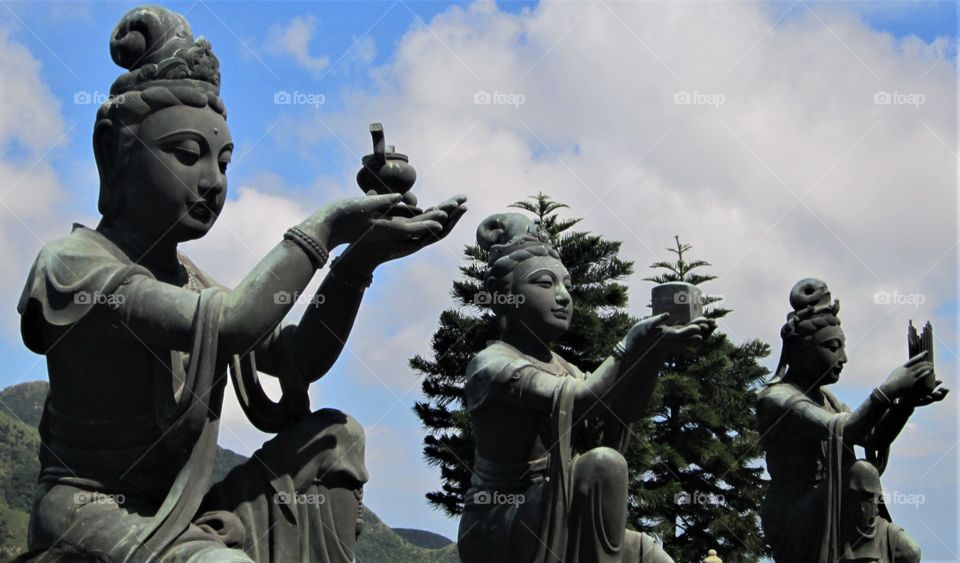 Three statues erected at the Po Lin Monastery in Hong Kong photographed on a clear summer’s day. A beautiful blue sky with fluffy white clouds in the background.