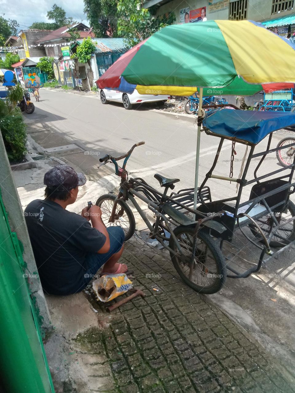 DRIVER IS FIXING HIS TRAYSIKAD( 3 WHEELS BICYCLE) FOR PUBLIC TRANSPORTATION, IS ANOTHER MEANS OF TRANSPORTING 2 PASSENGERS IN OUR LOCALITY,,