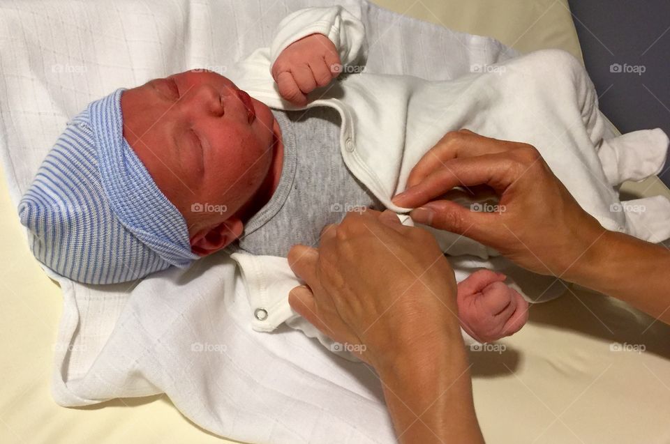 Person's hand wearing clothes to newborn baby