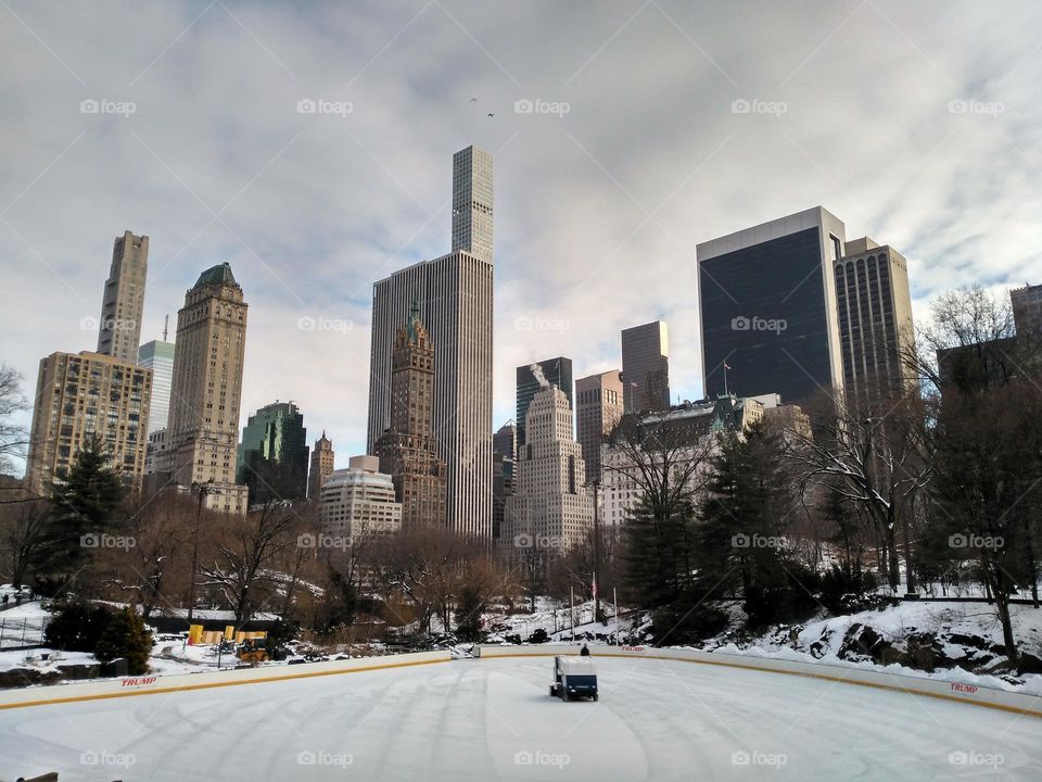 Ice skating rink in Central Park with city buildings in the background, winter day in New York, USA