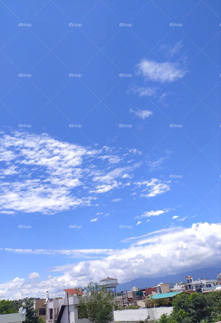 Flakes of white clouds floating across a beautiful blue sky over Mussoorie hills