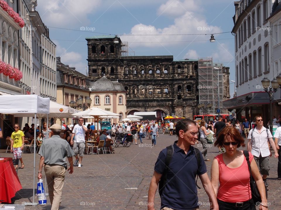 A busy town square with many tourists and an ancient building as the main attraction in the background on a sunny summer day. 