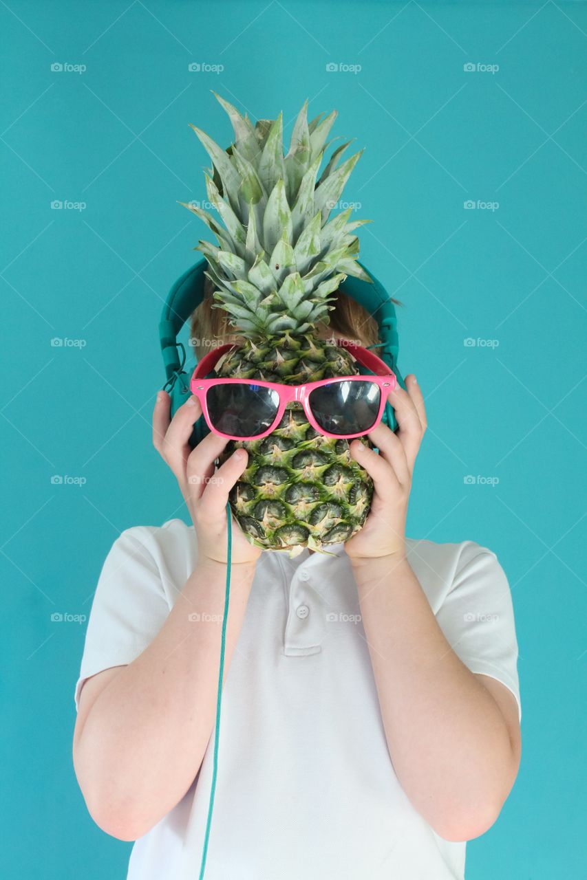 Teen holding up a pineapple wearing sunglasses and headphones