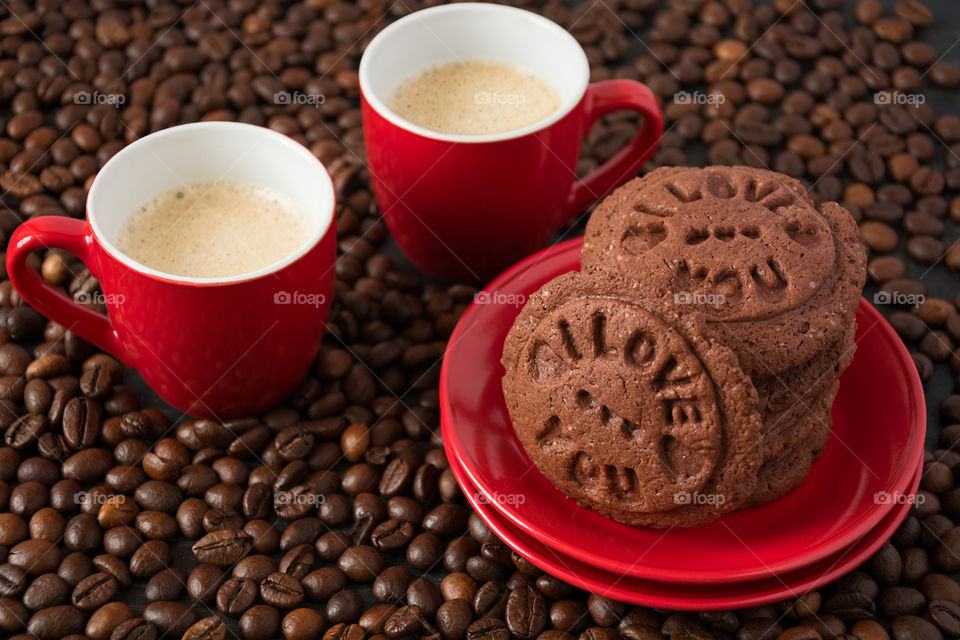 Two cups of espresso with chocolate cookies on coffee beans