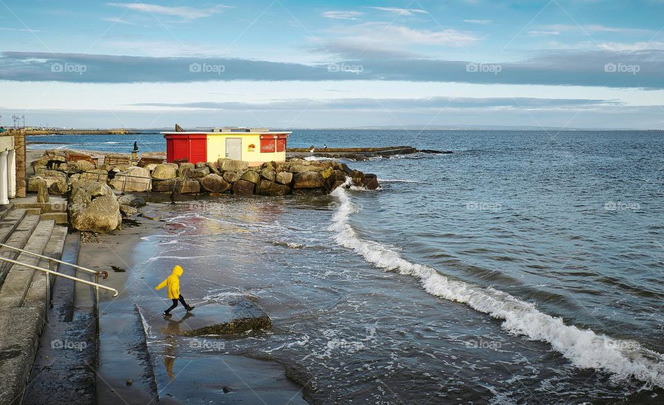 Kid in yellow jacket playing on sandy beach with beach house in the background at Salthill, Galway, Ireland