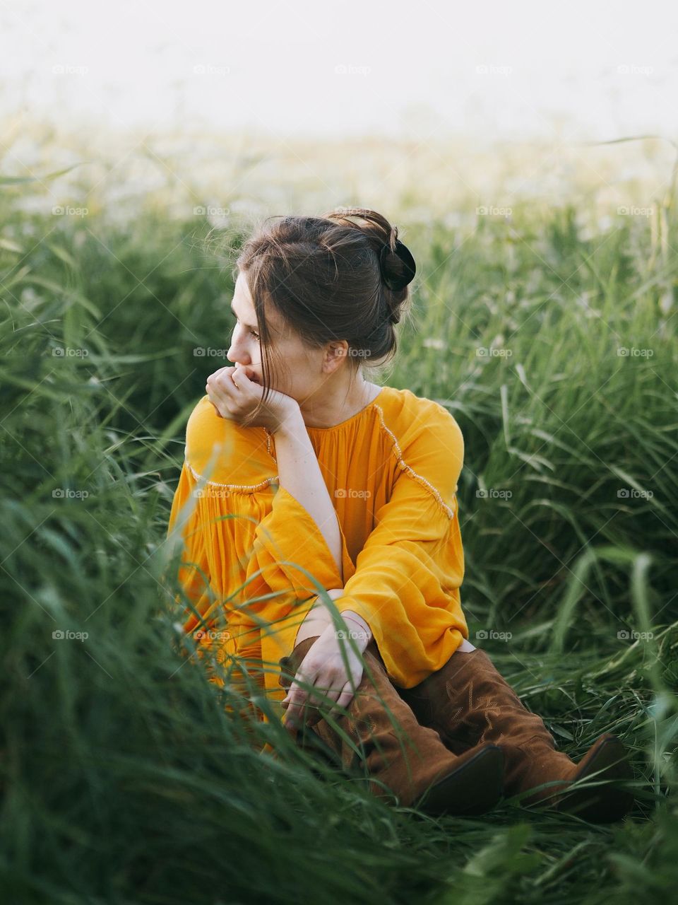 Young beautiful woman wearing yellow dress sitting on a green field in summer day