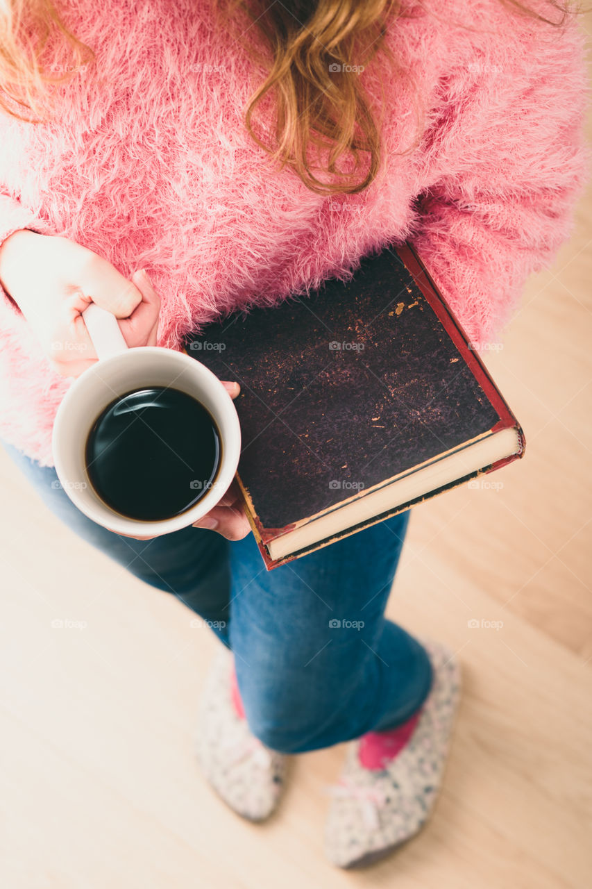 Enjoying the reading a book. Young girl holding book and cup of coffee going to relax with book. View from top