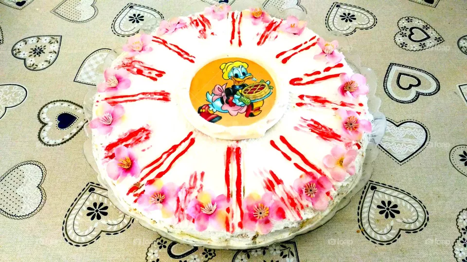 Disney theme birthday cake decorated with pink flowers on a grey heart-patterned tablecloth