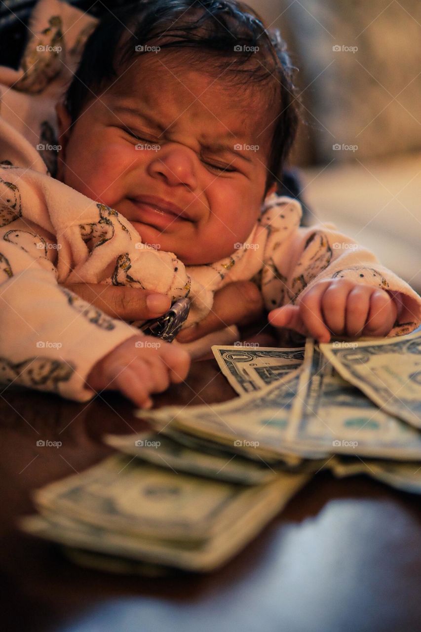 Baby’s face showing emotion of sadness, baby is crying and sad, baby is upset and sad, baby girl crying over money, baby and US money playing bingo, baby cries at losing bingo game, baby gambles