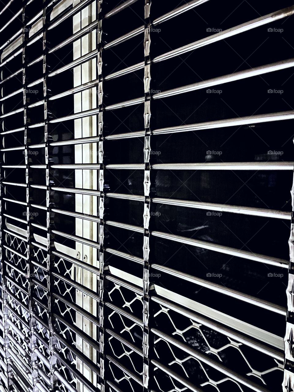 Silver/gold bars over a large window. The window is dark and reflects the street across from it. 