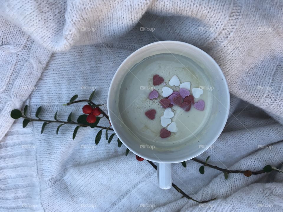 White hot chocolate in a white mug with a little pink and white hearts on top of it for a cozy and warm evening spent at home.