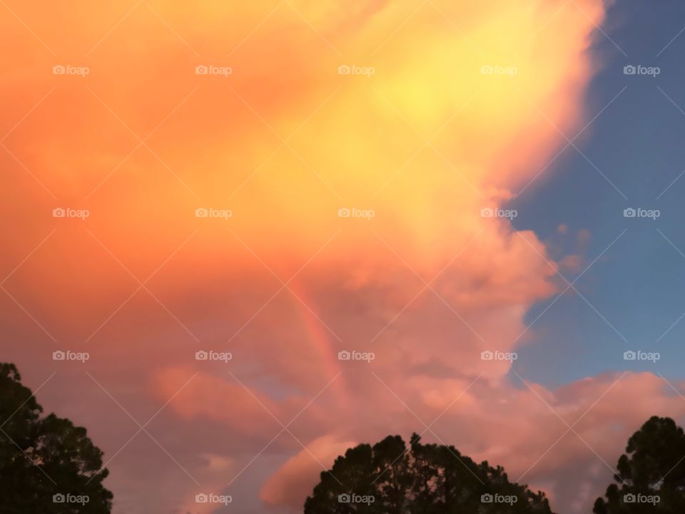 Blazing orange sunset with a rainbow after a storm.