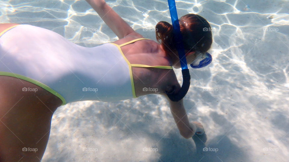 Young girl diving in the big blue sea with white sand