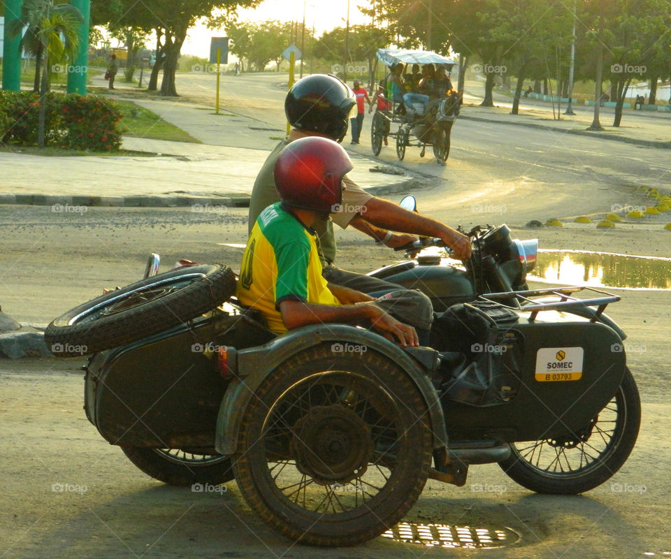Motorcycle with sidecar, Cuba. Two Cuban men in Santiago de Cubs on their way to work in a motorcycle and side car! All riders must wear a helmet.