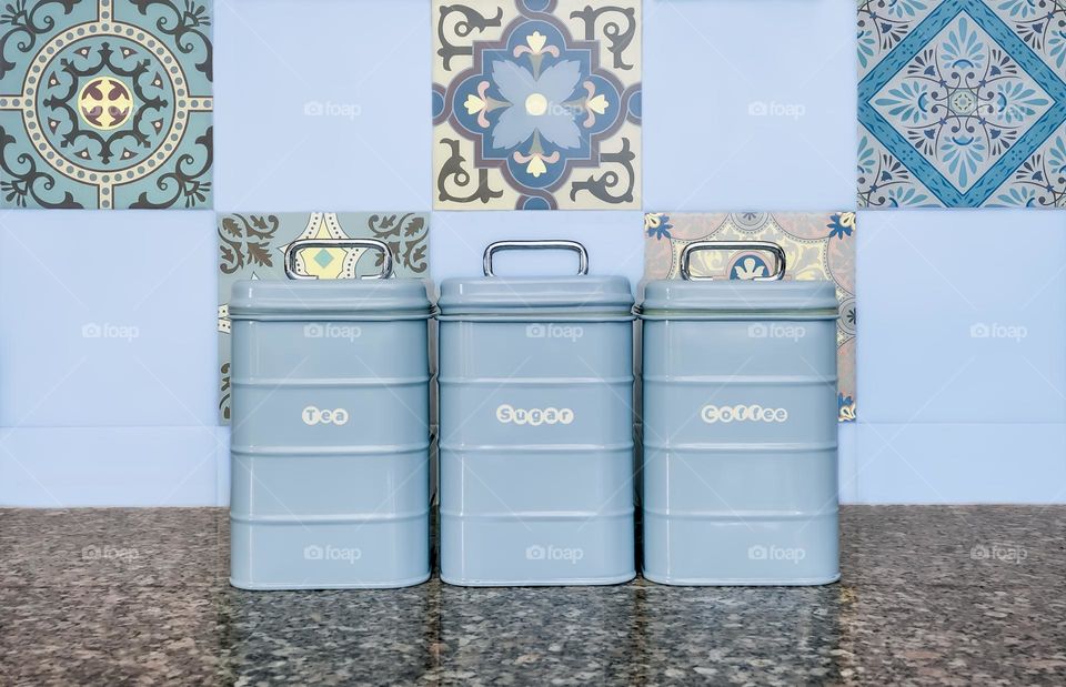 Rectangular metal storages canisters in front of a square tiled kitchen wall