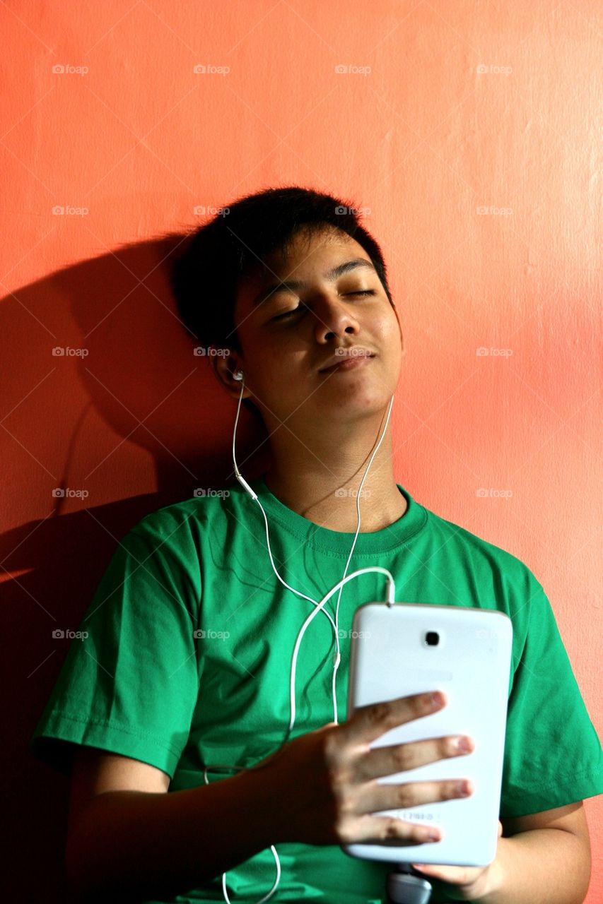 young asian teen listening to music on a tablet