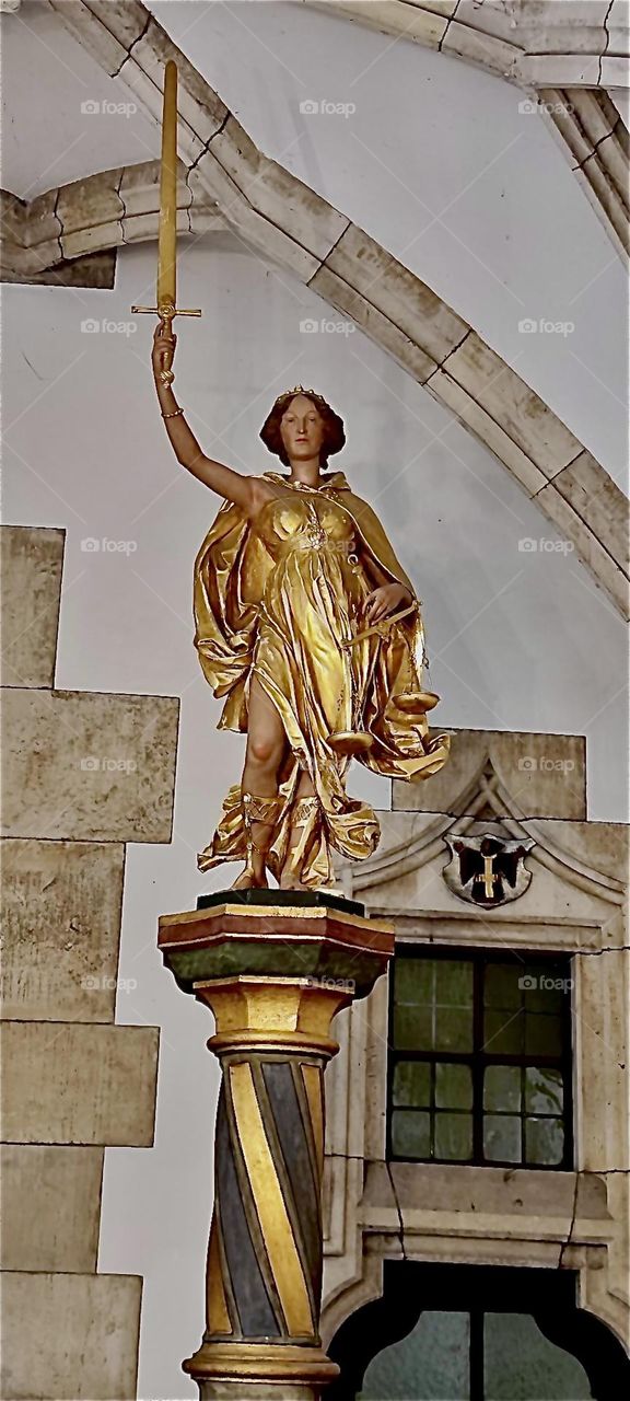 A golden statue of a beautiful lady adorns a hall inside the city hall of „Munich“ a.k.a. the „Rathaus“. It is housed inside a large multifaceted gothic style building that reminds more of a cathedral than a secular place. 2023. Hypnotic Productions