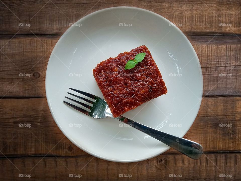 A slice of homemade coconut honey cake in a white ceramic plate, over wooden background top view .