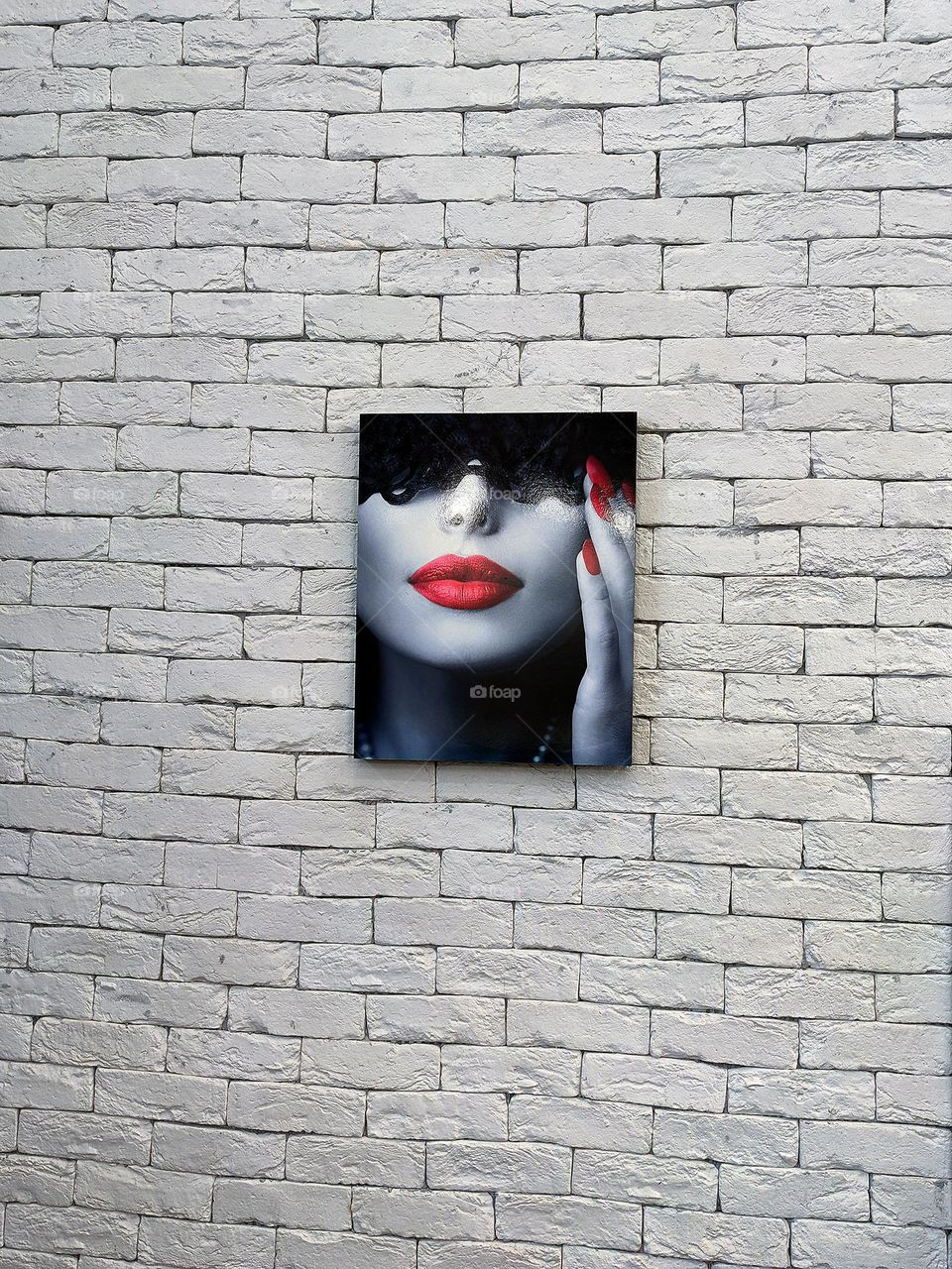 The minimalism of the object.  A multi-colored black and red portrait of a girl hangs on a white brick wall. Background and subject contrast