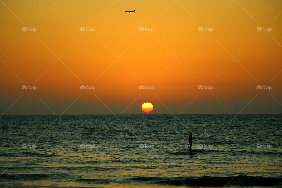 surfing at sunset. surfing With a plane flying and sun in the horizon