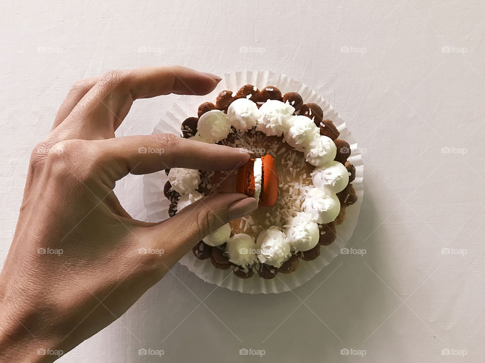 Female hand taking an orange macaroon from the top of fresh baked cupcake 