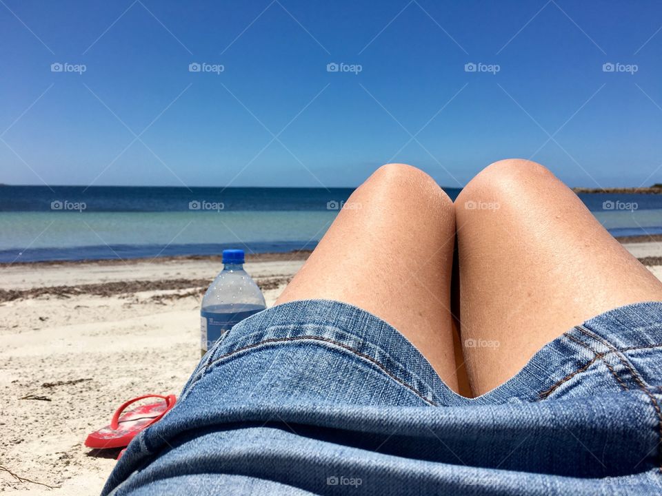 Paradise, woman in denim skirt and bare legs sitting on beach watching ocean, horizon, 