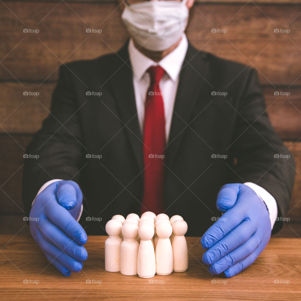 And employer or businessman wearing PPE face mask and blue protective gloves shielding his workers from coronavirus in a business and healthcare concept image