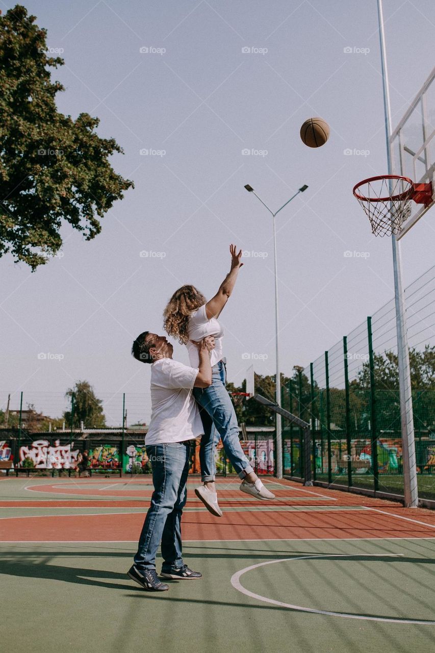 Boy and girl playing basketball. Boy help and holding girl
