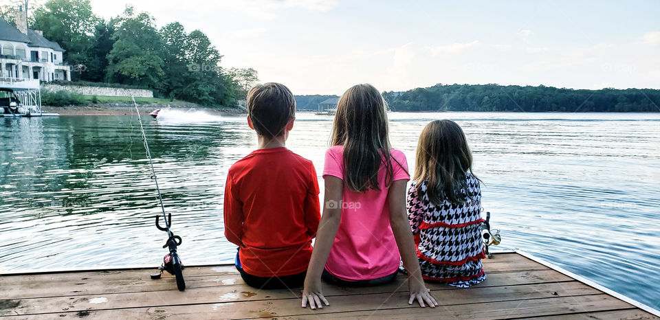 Three kids sitting on dock at lake...