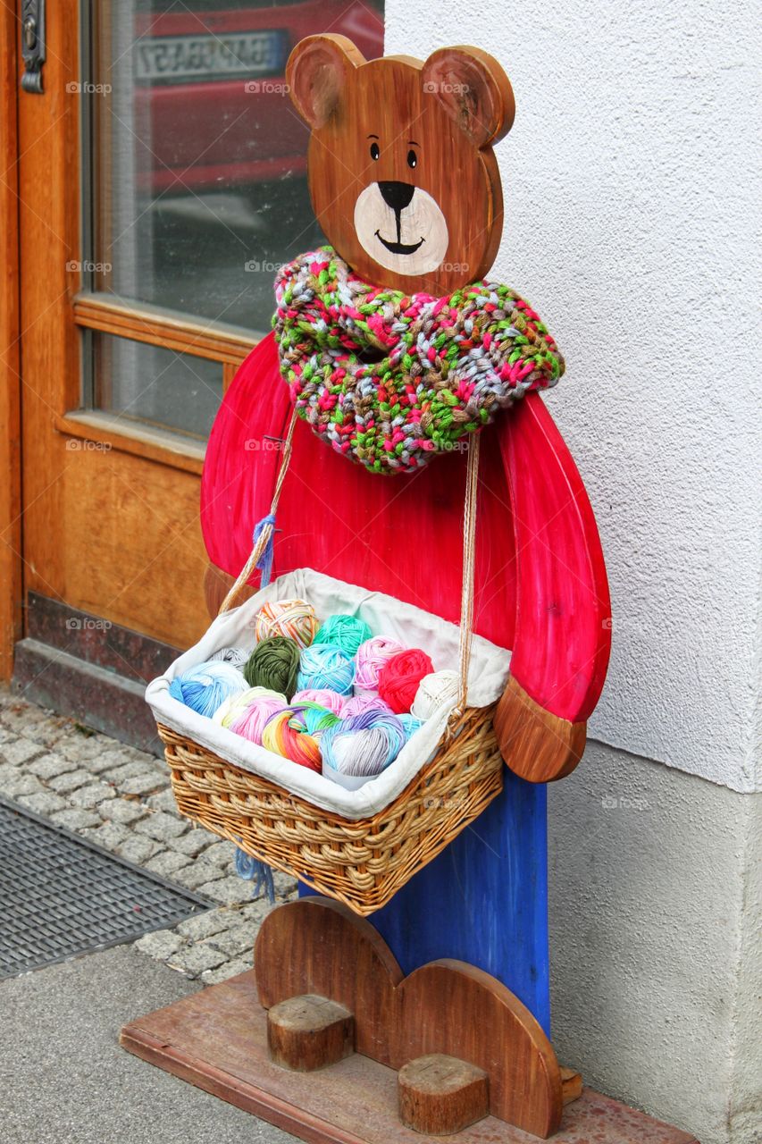 wooden figure of a bear with a bright knitted scarf and a basket of balls of woolen threads