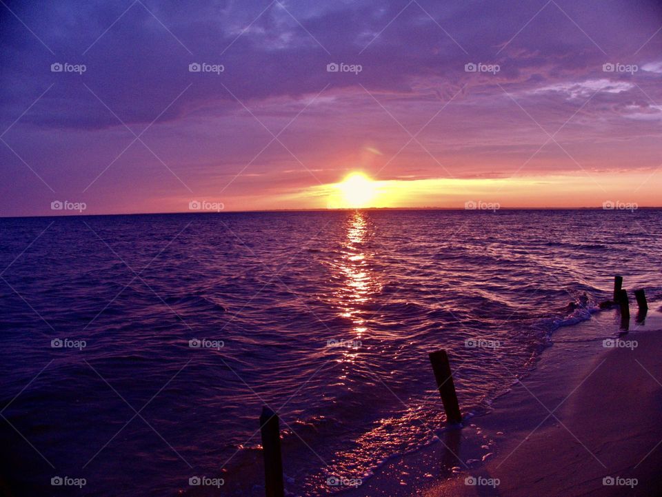 Ocean Reflection - The water reflects the colors of the sky, creating a mirrored effect and enhancing the overall vibrancy of the scene. The horizon line is clearly visible, separating the sky and the ocean, with the sun setting directly on it