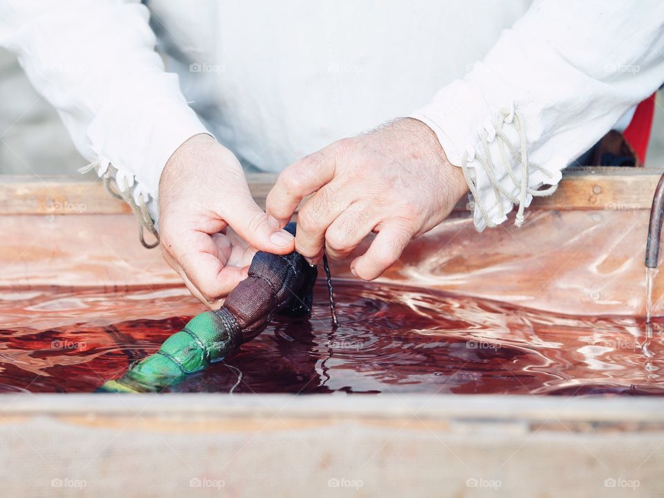 The man in the old national costume is showing a process of the hand dyeing fabric in Italy