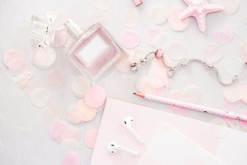 Flatlay items: reading glasses, wireless headphones, notebook, pencil, star pink color, confetti lying on gray concrete background 