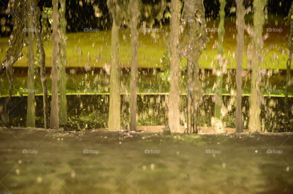 Closeup detail of water spray shooting up from fountain with green landscape background 