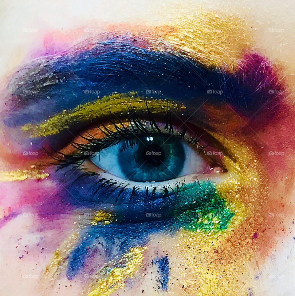 An extremely colourful makeup around a deep piercing blue eye. Long lashes, the eye looks feminine. It’s sparkling and vivid.