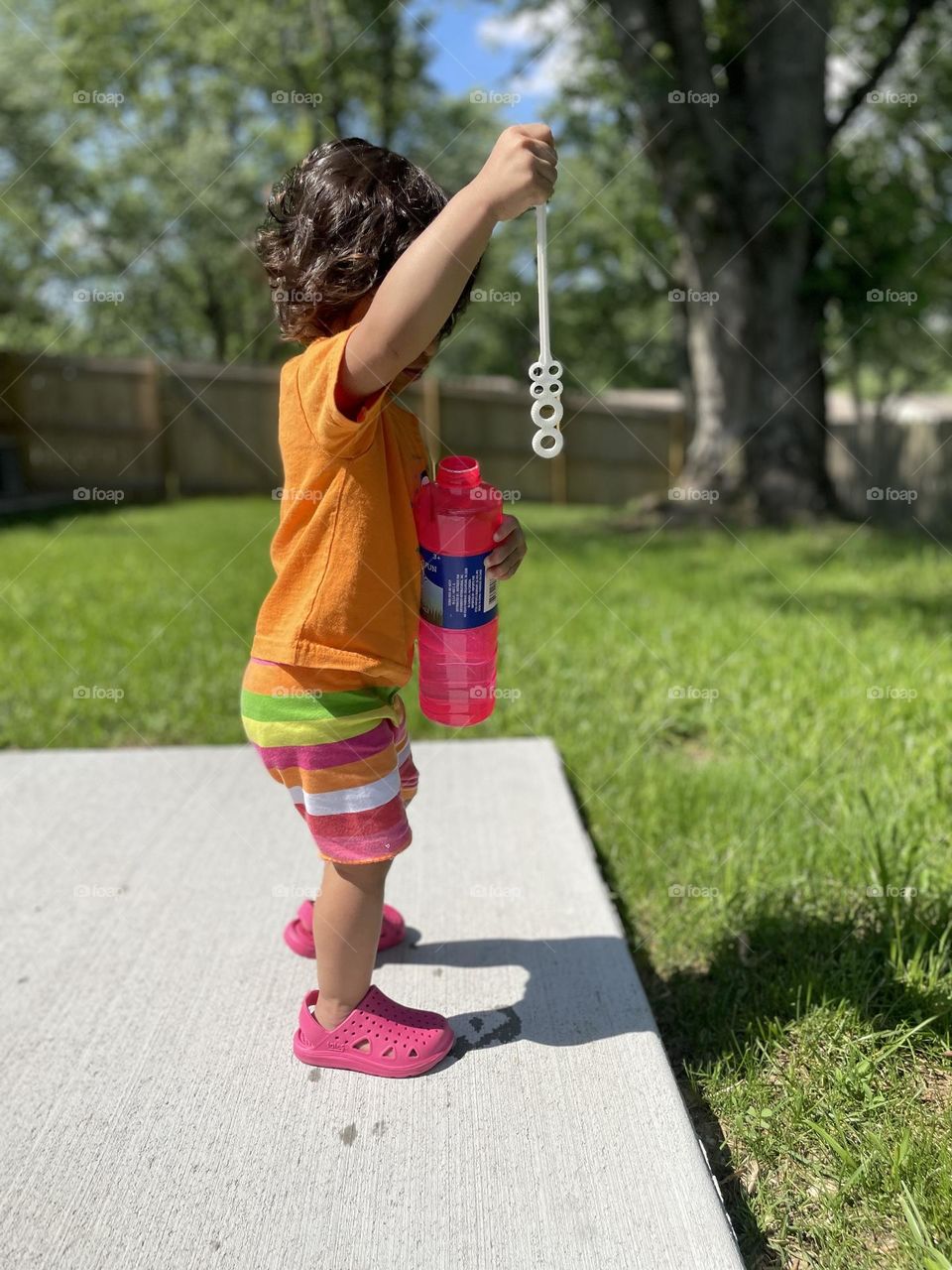 Toddler girl with bubbles in summertime outfit, summertime fun on the patio, child playing outside in a summertime outfit 