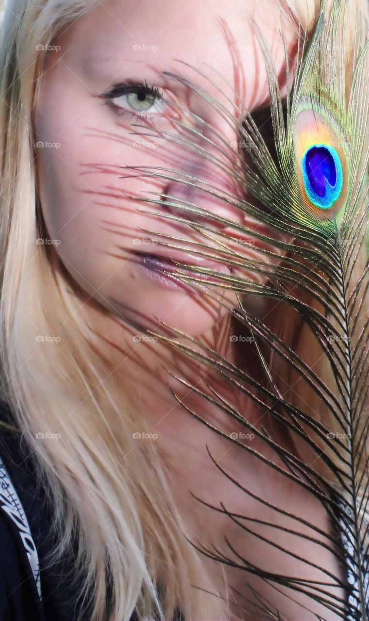 Young woman covering her face with peacock feather