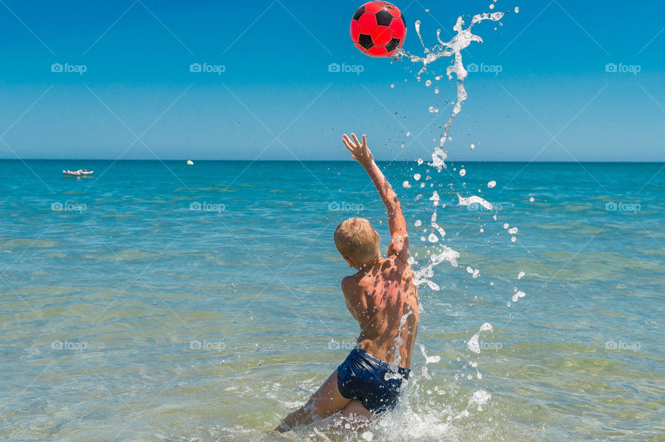 Boy is playing with red ball in the sea on the beach