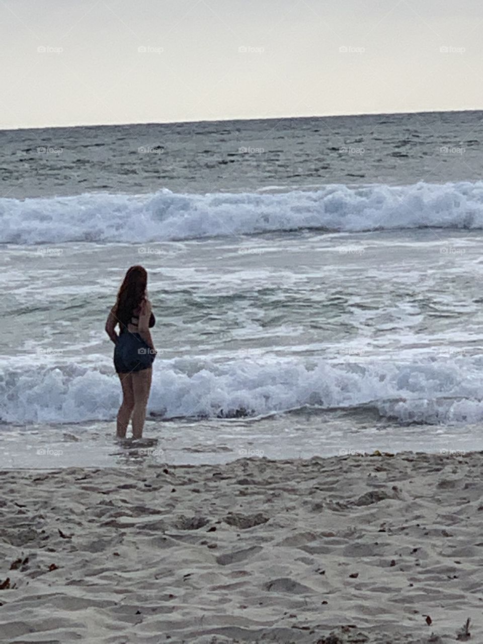 Girl standing with her feet in the water on an overcast day in the ocean 
