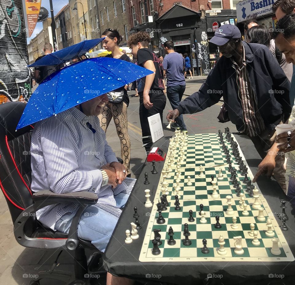 London, UK.  A chess master wearing a fanciful parasol hat takes on all comers.