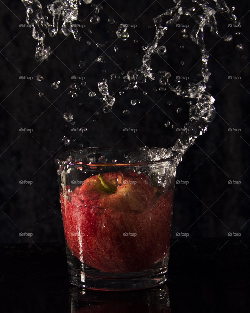 Fruit water splash,apple dropped into glass of water... black background 