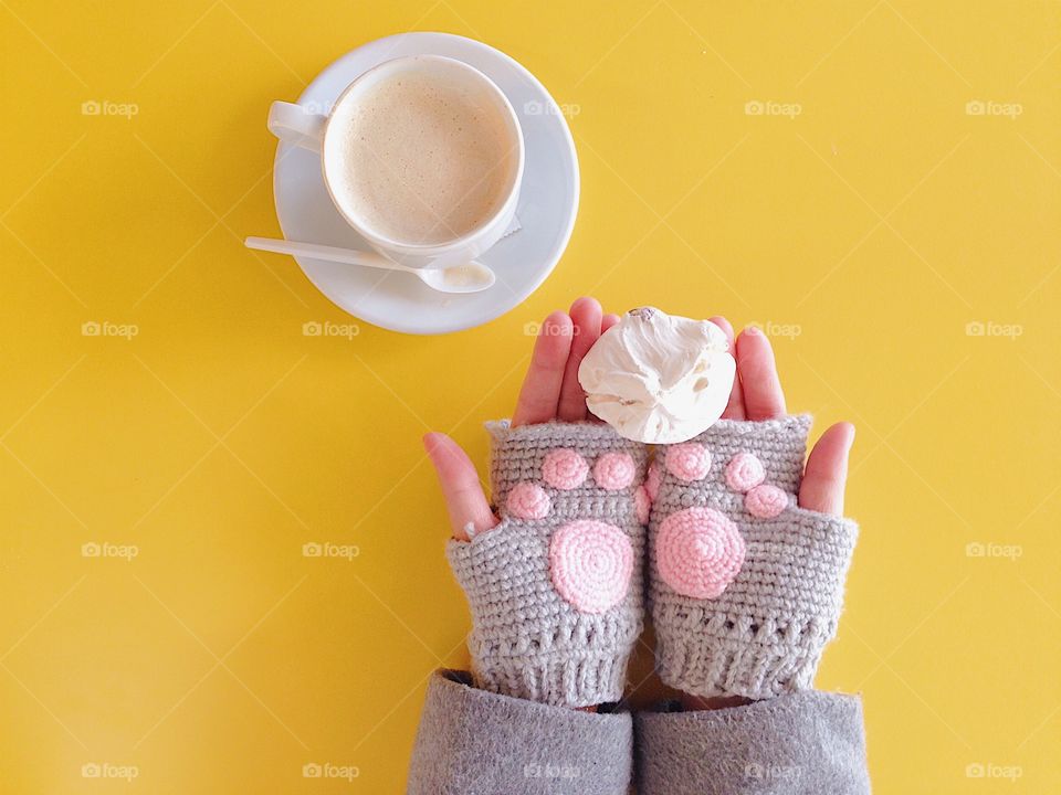 Hands holding meringue and hot chocolate. Hands wearing cute knitting fingerless gloves with cat paw in pink crochet. Warm and cozy concept. 