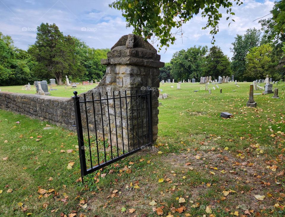 A weathered and beaten wrought iron gate hangs on tired hinges but still takes its job seriously as the gateway to the souls it safeguards in a old Midwest cemetery