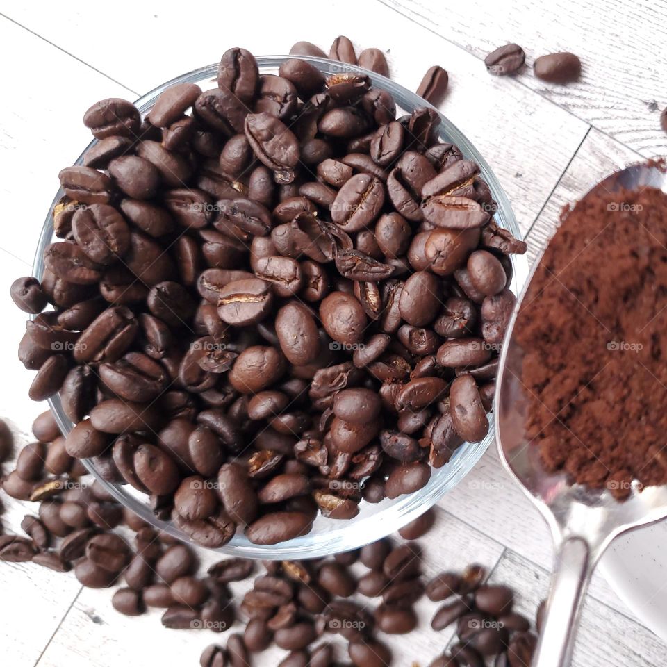 Coffee beans on a  bowl and freshly grounded coffee beans on a spoon.