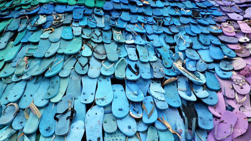 Portrait of piles of colorful flip-flops that are neatly arranged and look aesthetically pleasing, dominated by blue sandals.